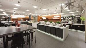 Ein modernes Restaurant mit einer zentralen Kochinsel, Sitzbereich und einer Küche im Hintergrund.