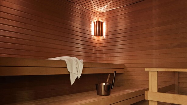 Eine Sauna mit Holzbänken, einem Metallkübel und einem Handtuch an der Wand.