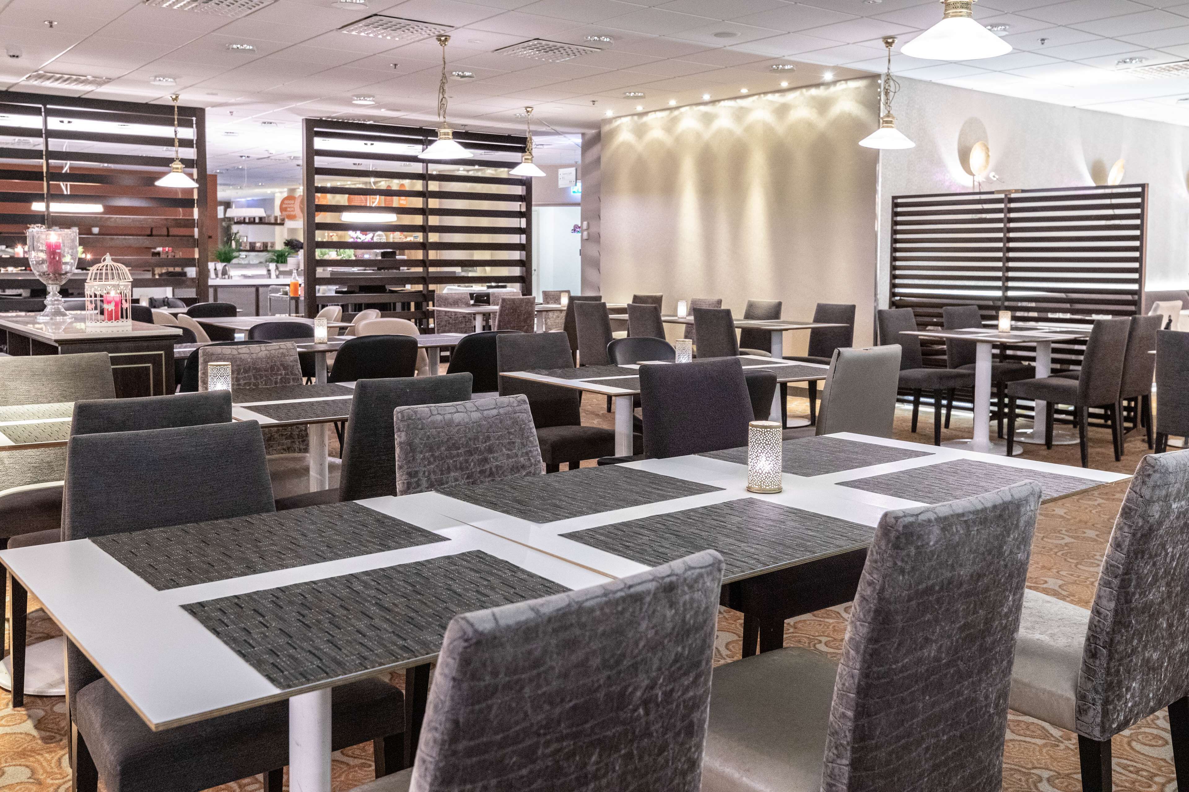 Un restaurant moderne doté de nombreuses tables et chaises, et présentant un design contemporain caractérisé par un mélange de couleurs foncées et claires.