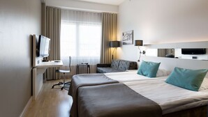 Ein Hotelzimmer mit zwei Betten, einem Schreibtisch, einem Stuhl, einem Fernseher und einem Fenster mit Vorhängen.