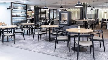 Un interior de restaurante moderno con mesas redondas, sillas negras e iluminación colgante.