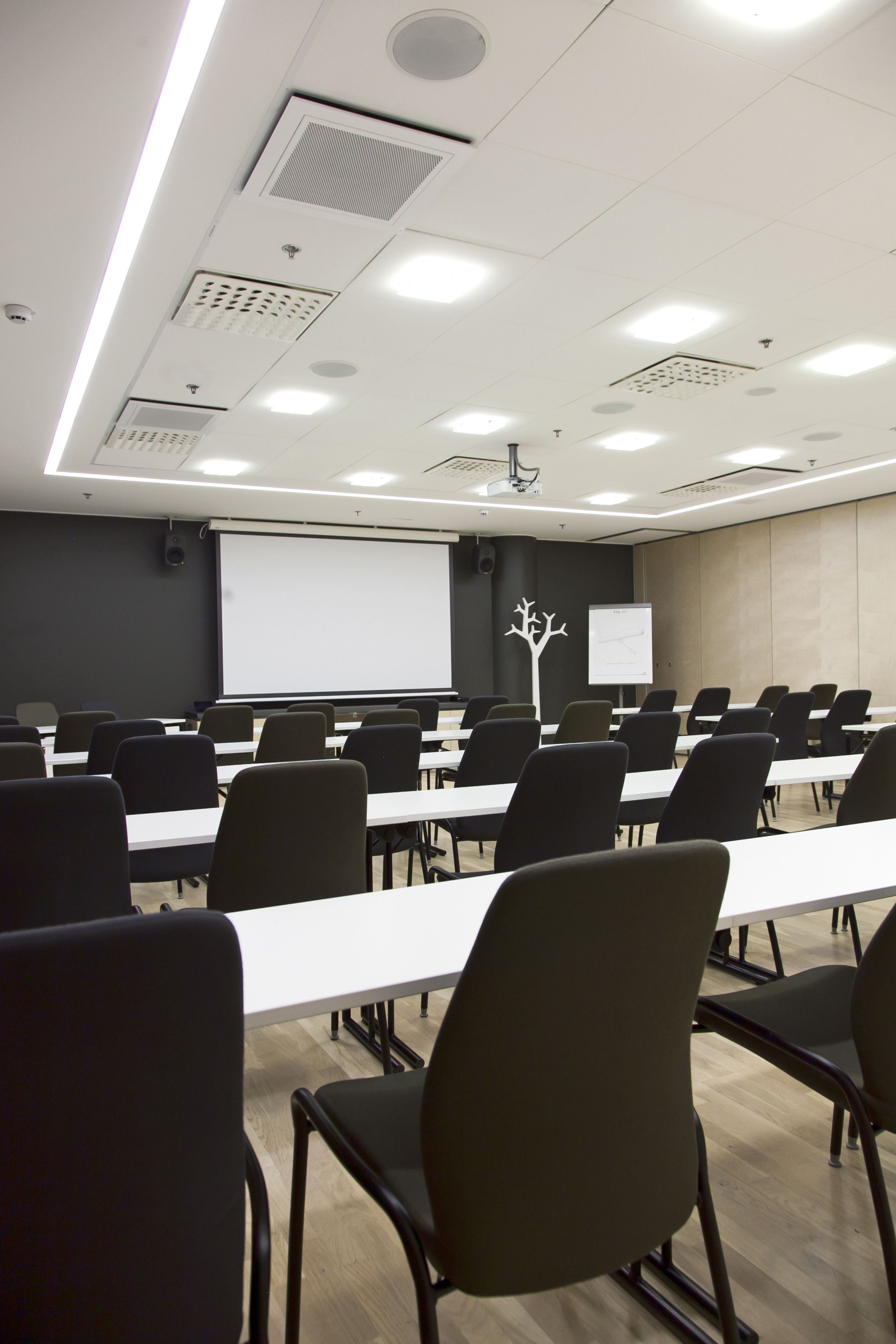 A conference room with rows of tables and chairs, a projector screen, and a whiteboard.