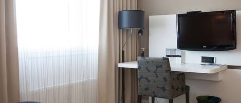 Una habitación de hotel con una cama, un escritorio con silla, un televisor, una lámpara y un cesto de basura.
