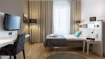 Quarto de hotel com cama, escrivaninha, cadeira, televisão e janela com cortinas.