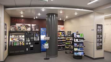 A modern retail area with a 'SHOP' sign, vending machines, and shelves stocked with various products.
