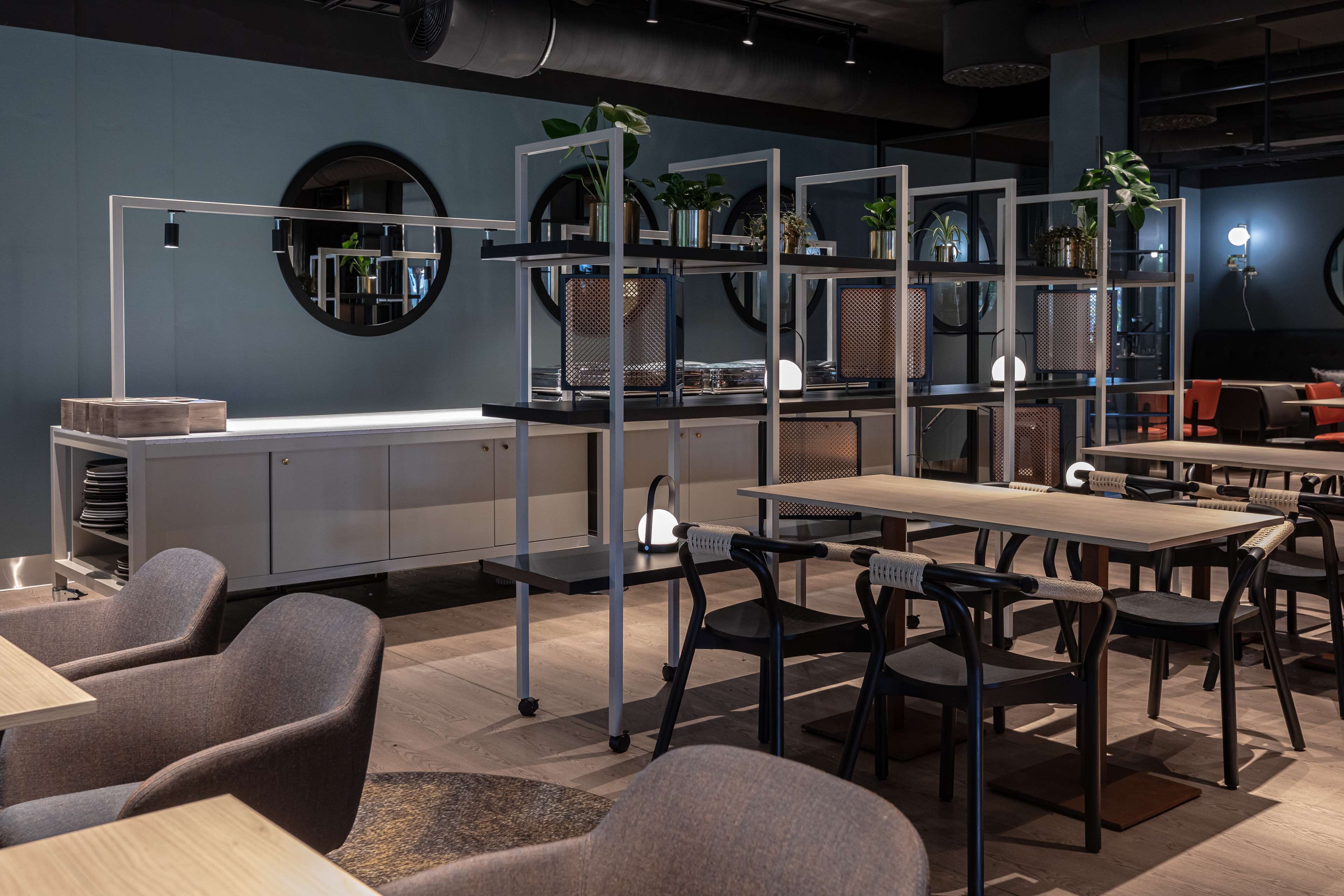 A modern restaurant with a central dining area, high chairs, and a counter with plants.