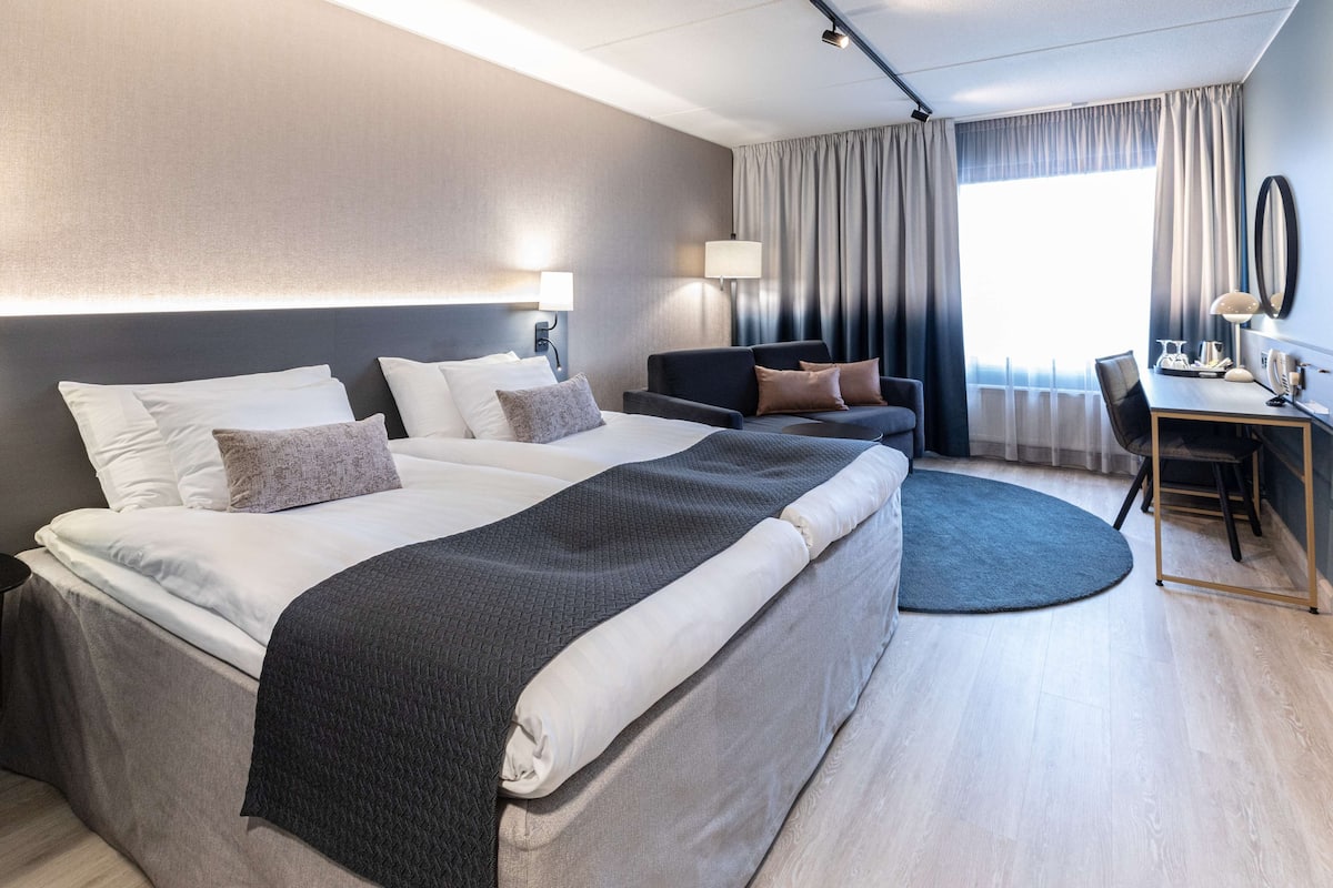 A modern hotel room with a large bed, a desk, and a chair.