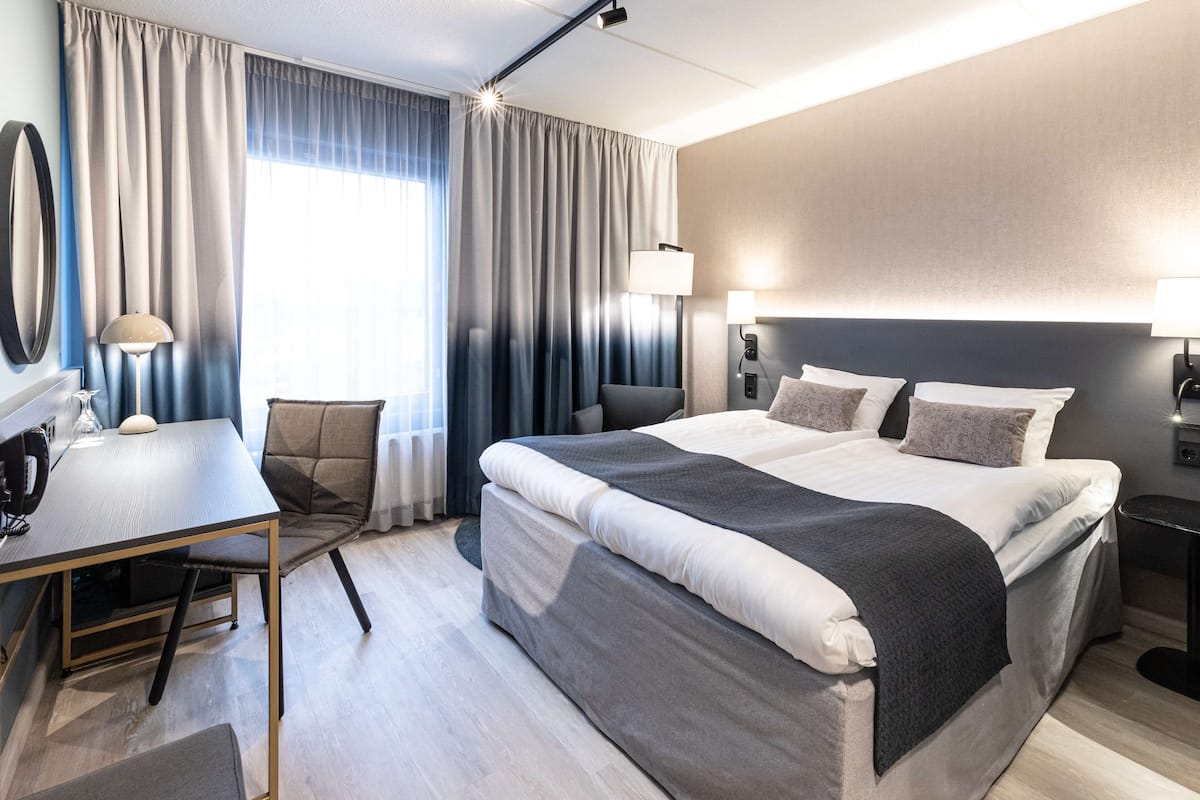 A modern hotel room with a large bed, a desk, and a chair.