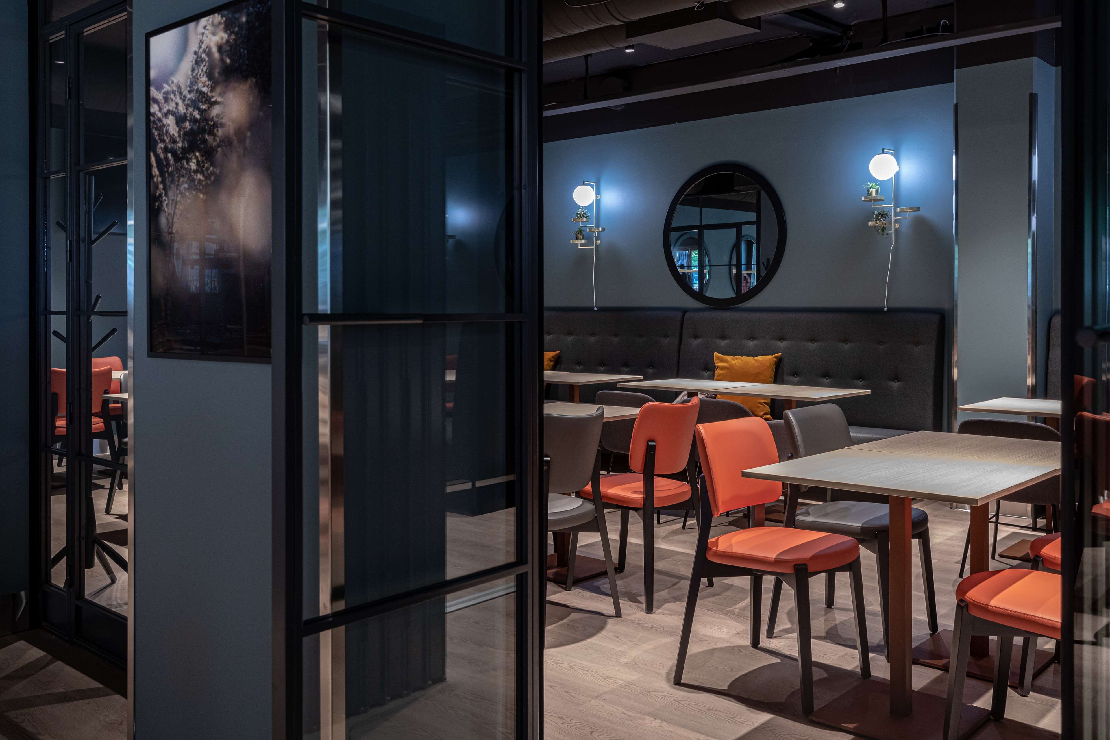 A modern restaurant with a grey sofa, orange chairs, and tables.