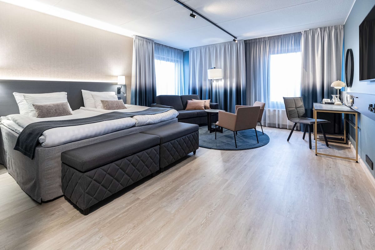 A modern hotel room with a large bed, a sofa, a desk, and a chair.