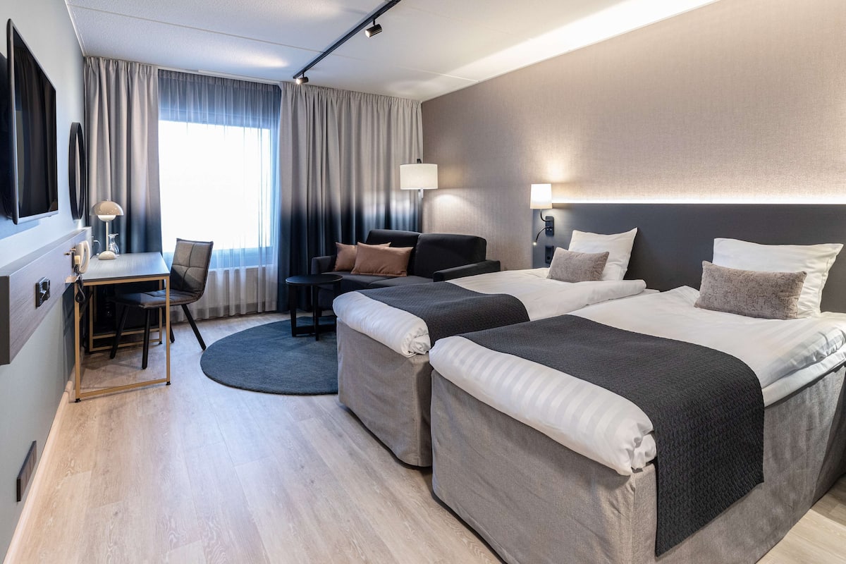 A modern hotel room with two beds, a desk, and a chair.