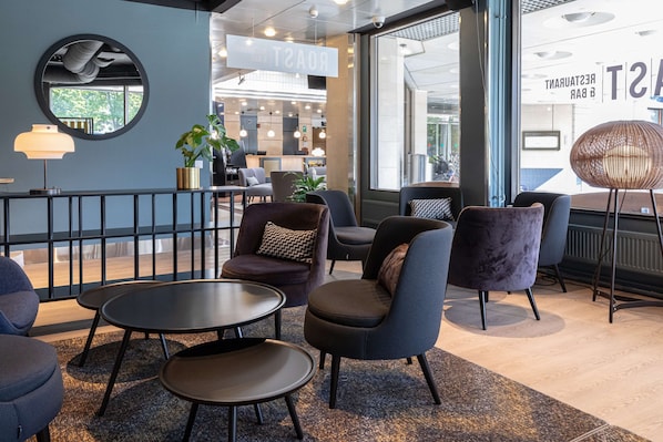 A modern lounge area with comfortable seating, a round mirror, and a view of the restaurant area.