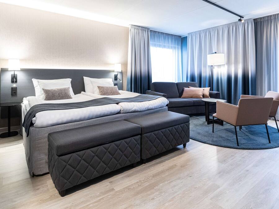 A modern hotel room with a large bed, a sofa, a small table, and a chair.