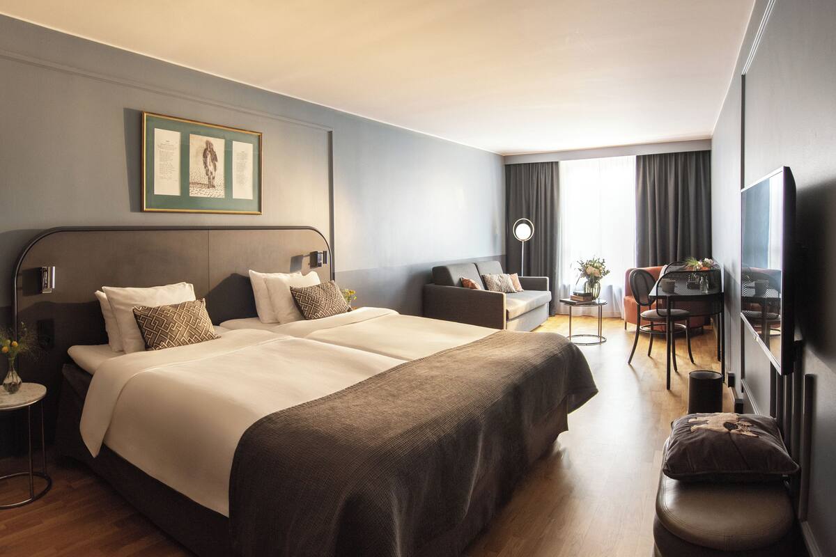 A hotel room with a large bed, a desk, a chair, and a television.