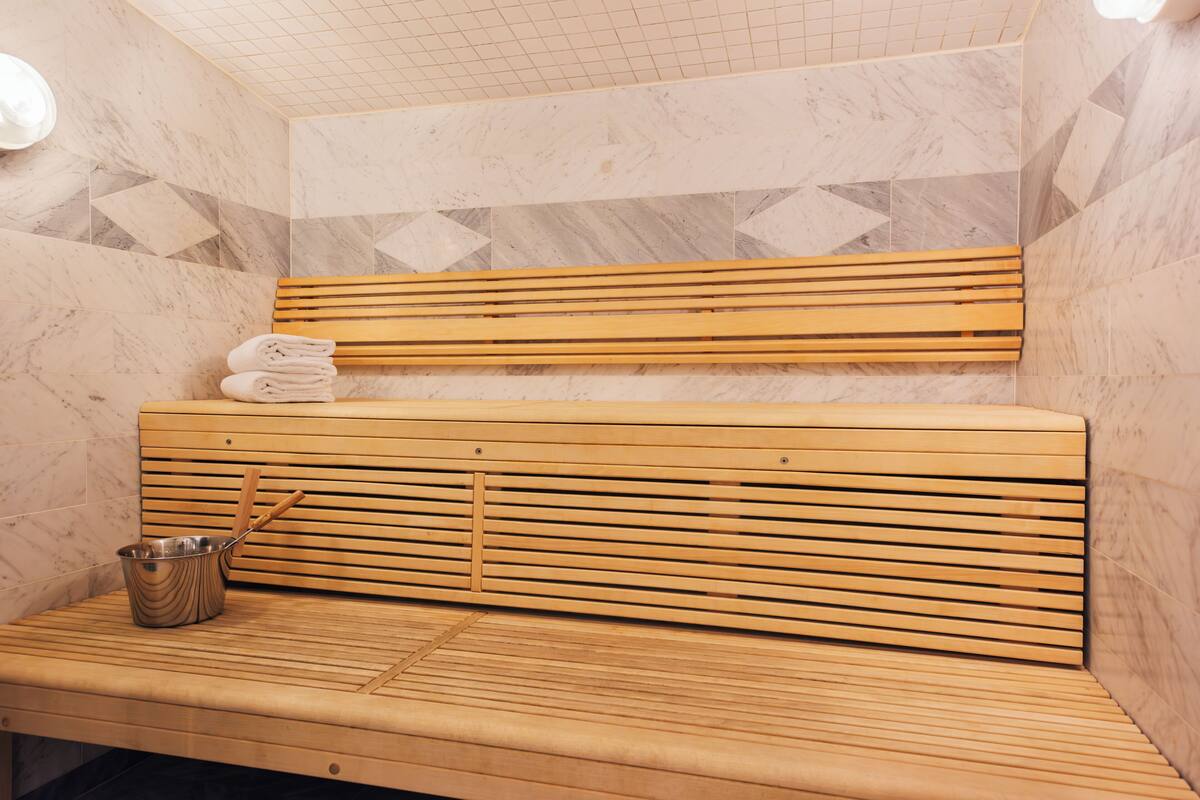 A sauna with wooden benches, a metal bucket, and towels.