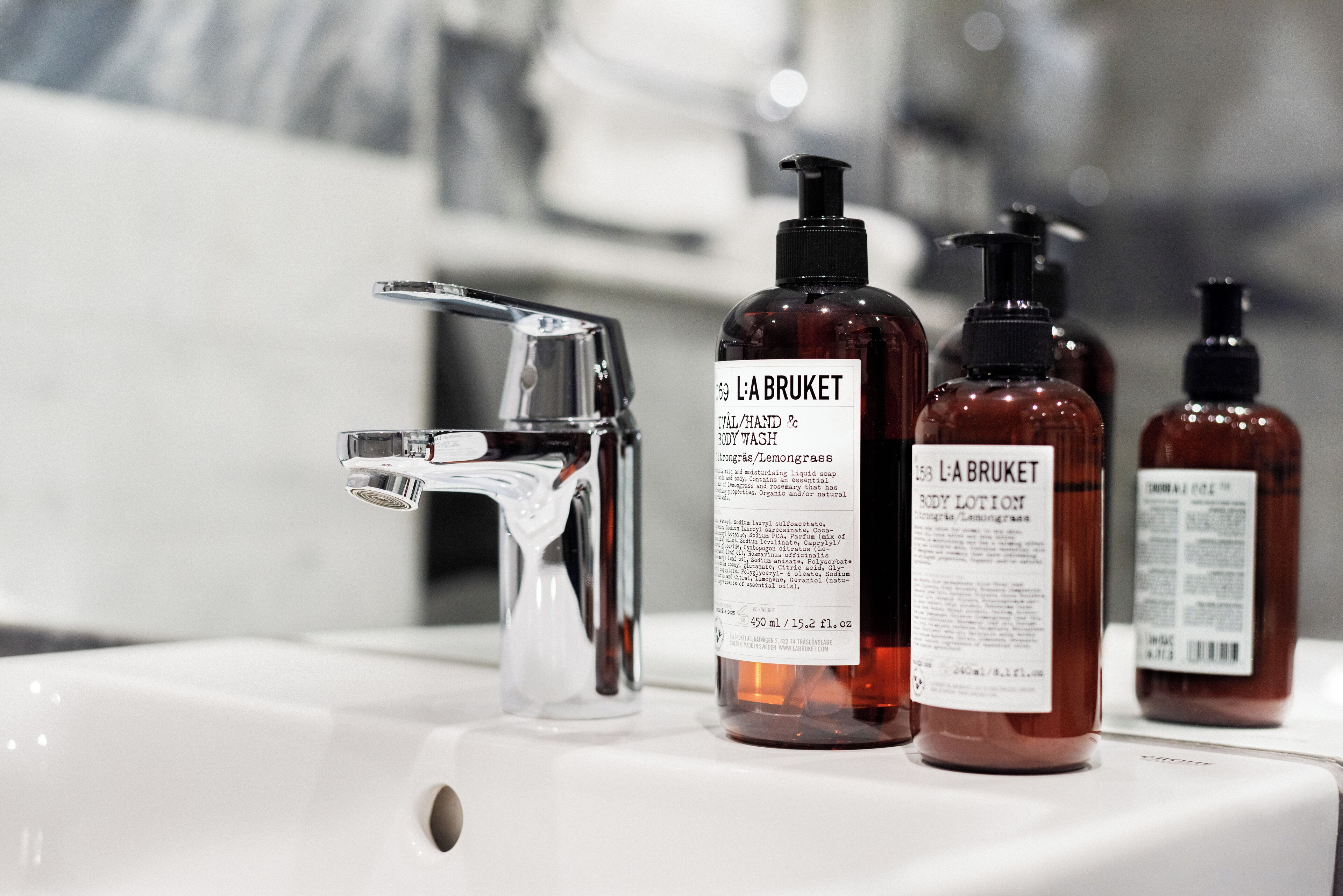 A bathroom sink with three bottles of L'A BRUKET body wash and lotion.