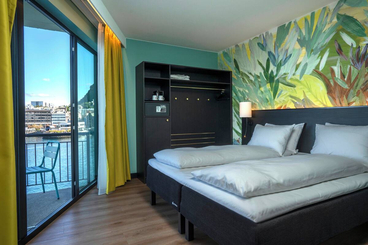 Ein Hotelzimmer mit Bett, Kleiderschrank, Balkon mit Stuhl und Blick auf die Stadt.