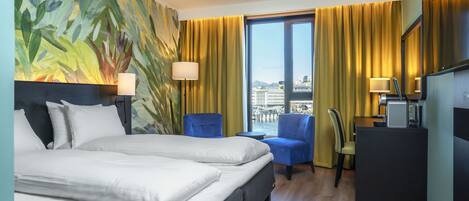 Una habitación de hotel con una cama, dos sillas, un escritorio y un ventanal con cortinas.