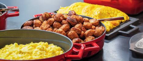 Una mesa de buffet con diversos alimentos, incluyendo huevos revueltos, pollo frito y tocino.