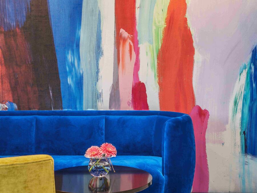 Una habitación con un sofá azul, un sillón amarillo y una mesa redonda con un jarrón de flores.