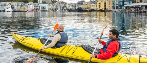 Dos personas haciendo kayak en un río tranquilo, con un pueblo al fondo.