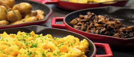 Three red skillets with different dishes: scrambled eggs, roasted potatoes, and sautéed mushrooms.