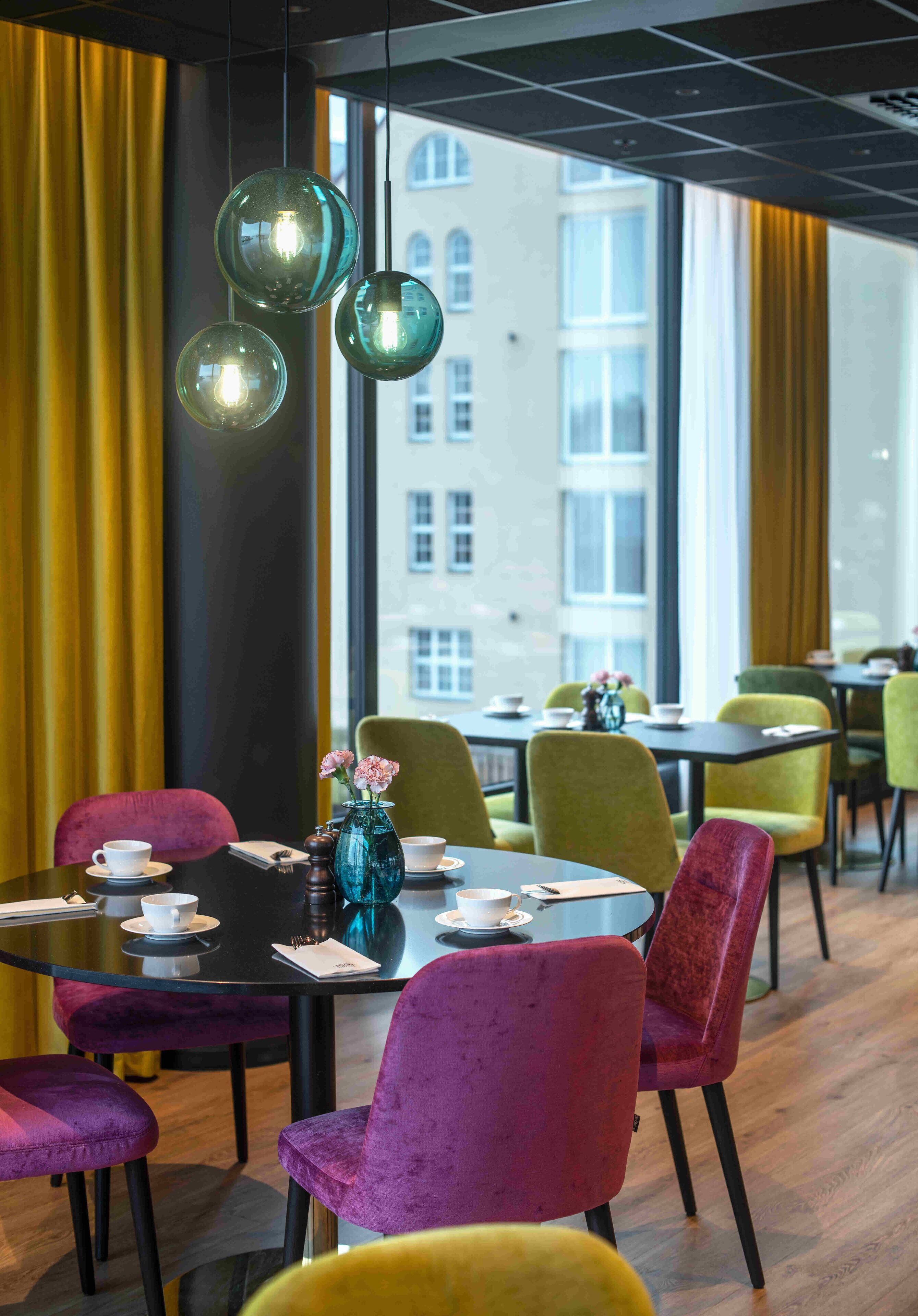A dining area with round tables, colorful chairs, and hanging glass lamps.