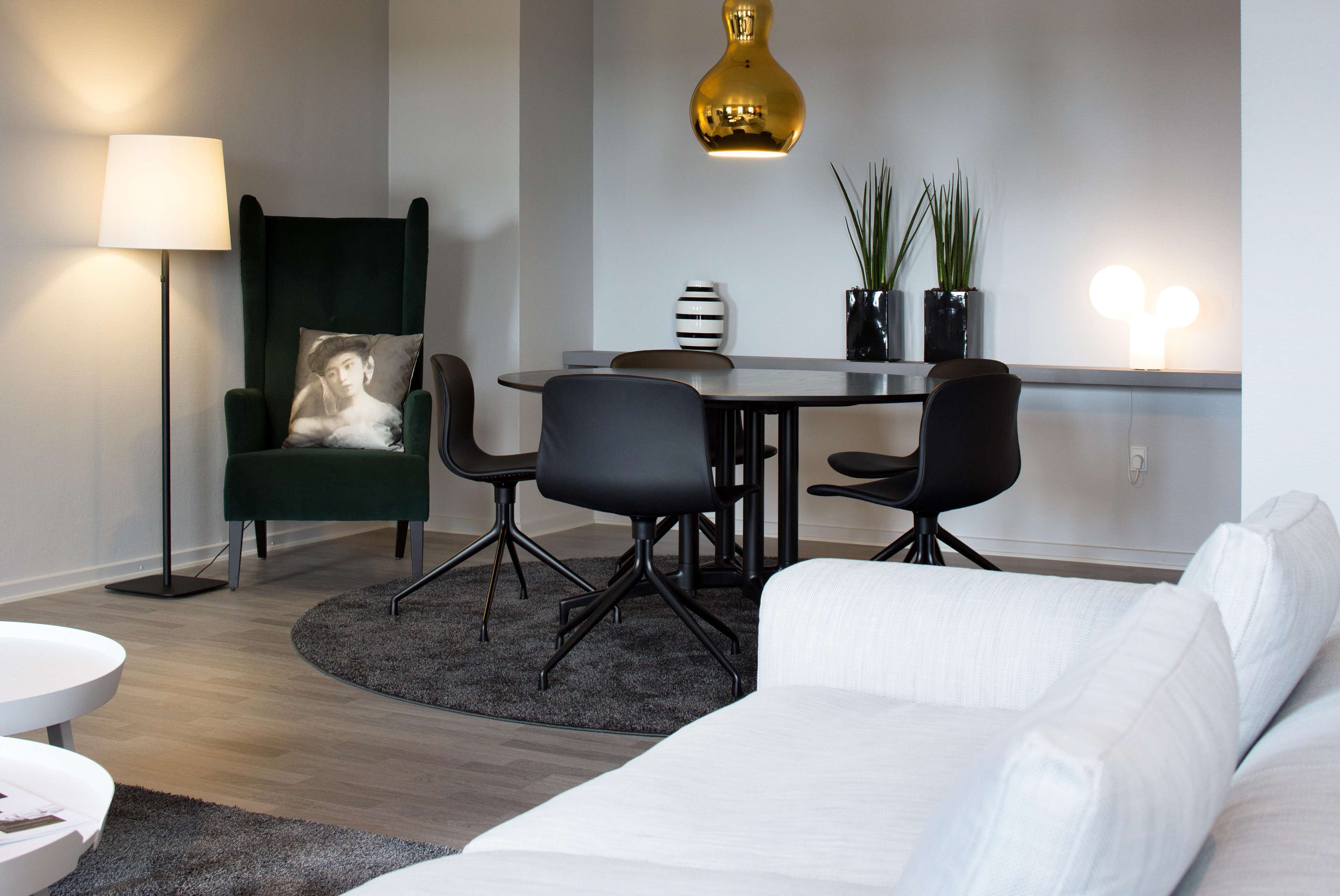 En moderne stue med en grøn lænestol, en hvid sofa, et spisebord med stole, en gulvlampe og en pendel.