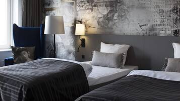 A hotel room with two beds, a blue armchair, a lamp, and a wall with a vintage map design.