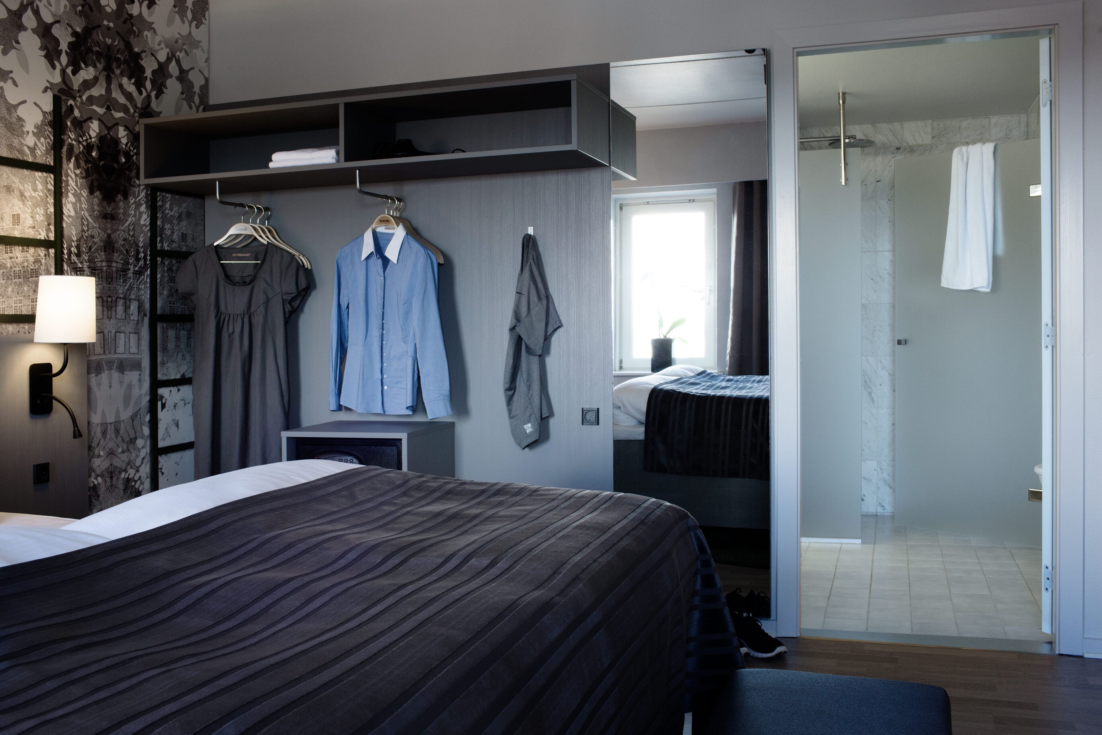 Ein modernes Schlafzimmer mit einem großen Bett, einem Kleiderschrank mit Kleidung, einem Nachttisch und einem Duschbereich.