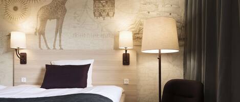 A hotel room with a bed, two wall-mounted lamps, a map-themed wall, and a chair.