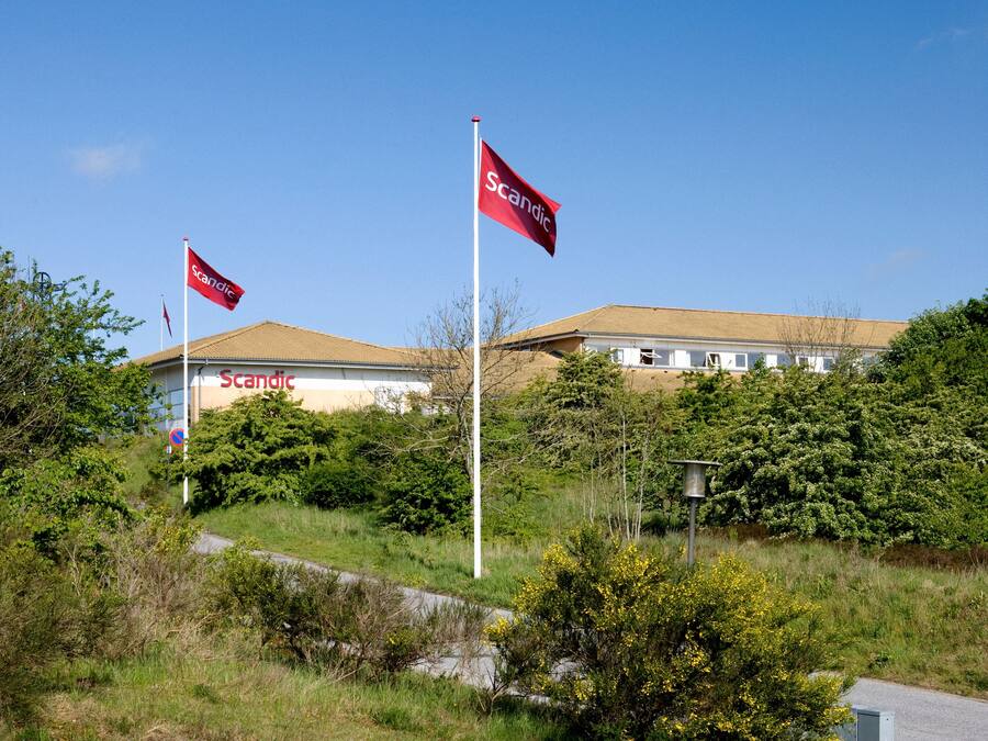A building with a clear blue sky, two red flags with the word "Scandic" on them, and a no parking sign.