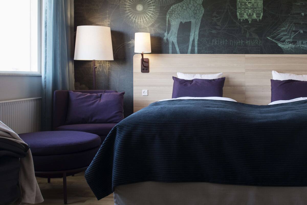 Hotellihuone, jossa on sänky, tuoli ja lamppu.