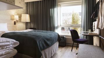Habitación de hotel con cama, escritorio, silla y ventana con cortinas.