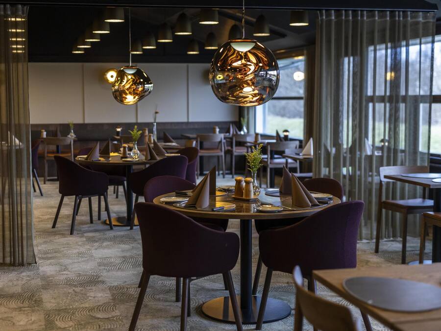 A modern restaurant interior with round tables, purple chairs, and hanging spherical light fixtures.