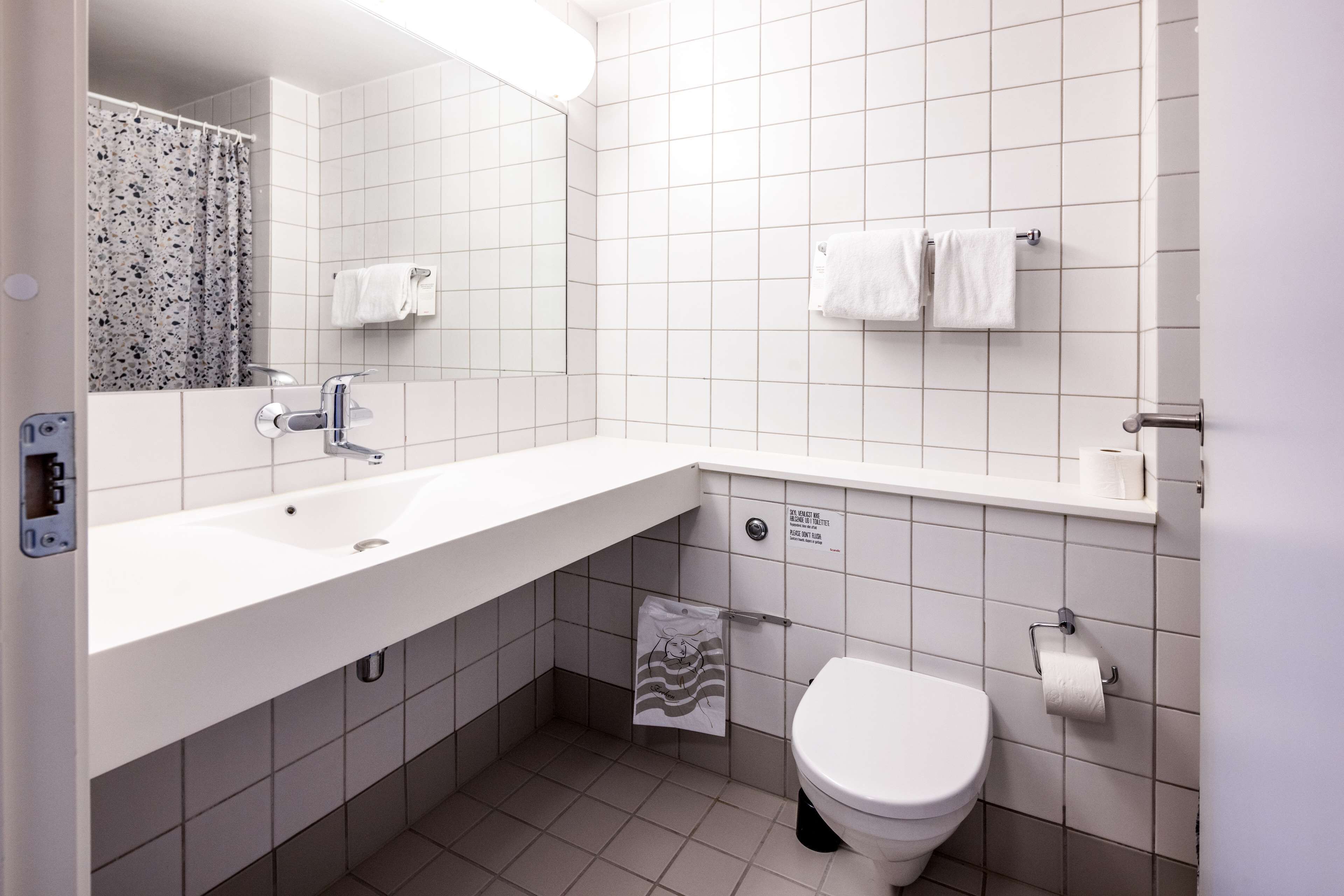 A modern bathroom with a white sink, mirror, and toilet. There are two towels hanging on the wall and a shower curtain with a floral pattern.