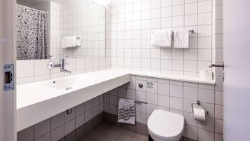 A modern bathroom with a white sink, mirror, and toilet. There are two towels hanging on the wall and a shower curtain with a floral pattern.