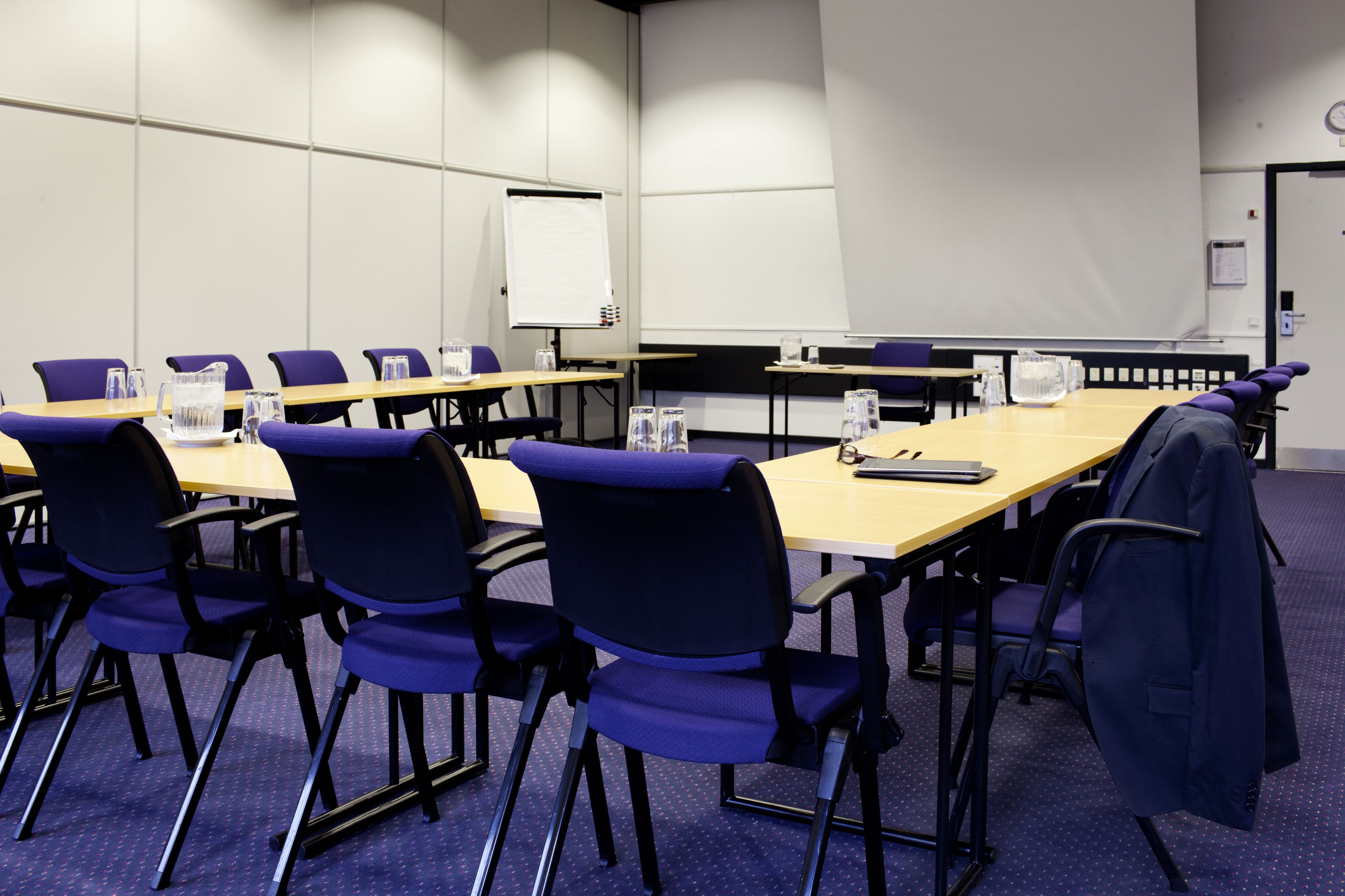 Une salle de conférence équipée d’une longue table, de chaises, d’un tableau blanc et d’un écran de projection.