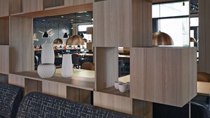 A modern interior with wooden shelving units, pendant lighting, and a seating area with patterned cushions. - Scandic Aarhus Vest (Aarhus)