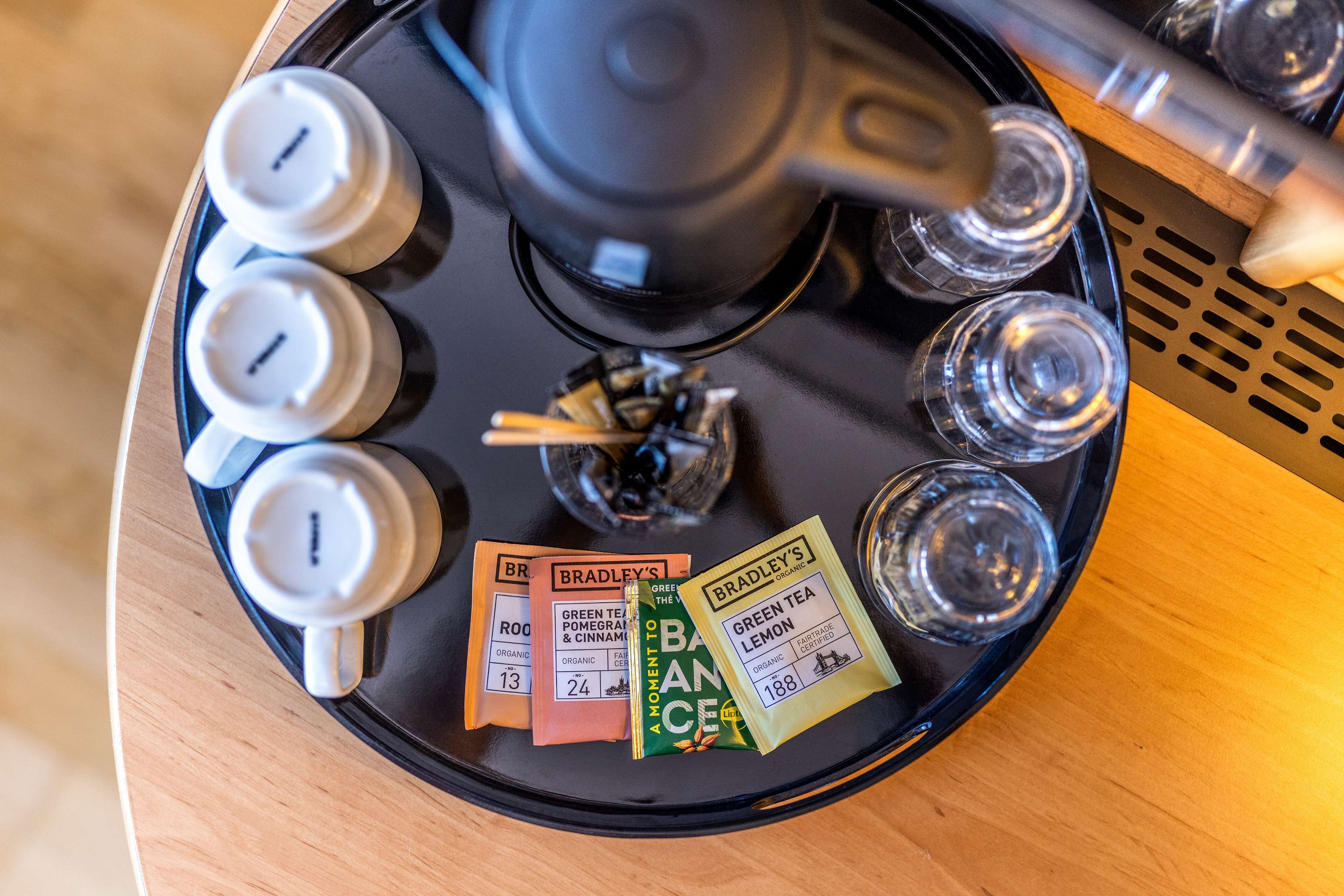 Una bandeja con bolsitas de té, una tetera y una taza sobre una mesa de madera.