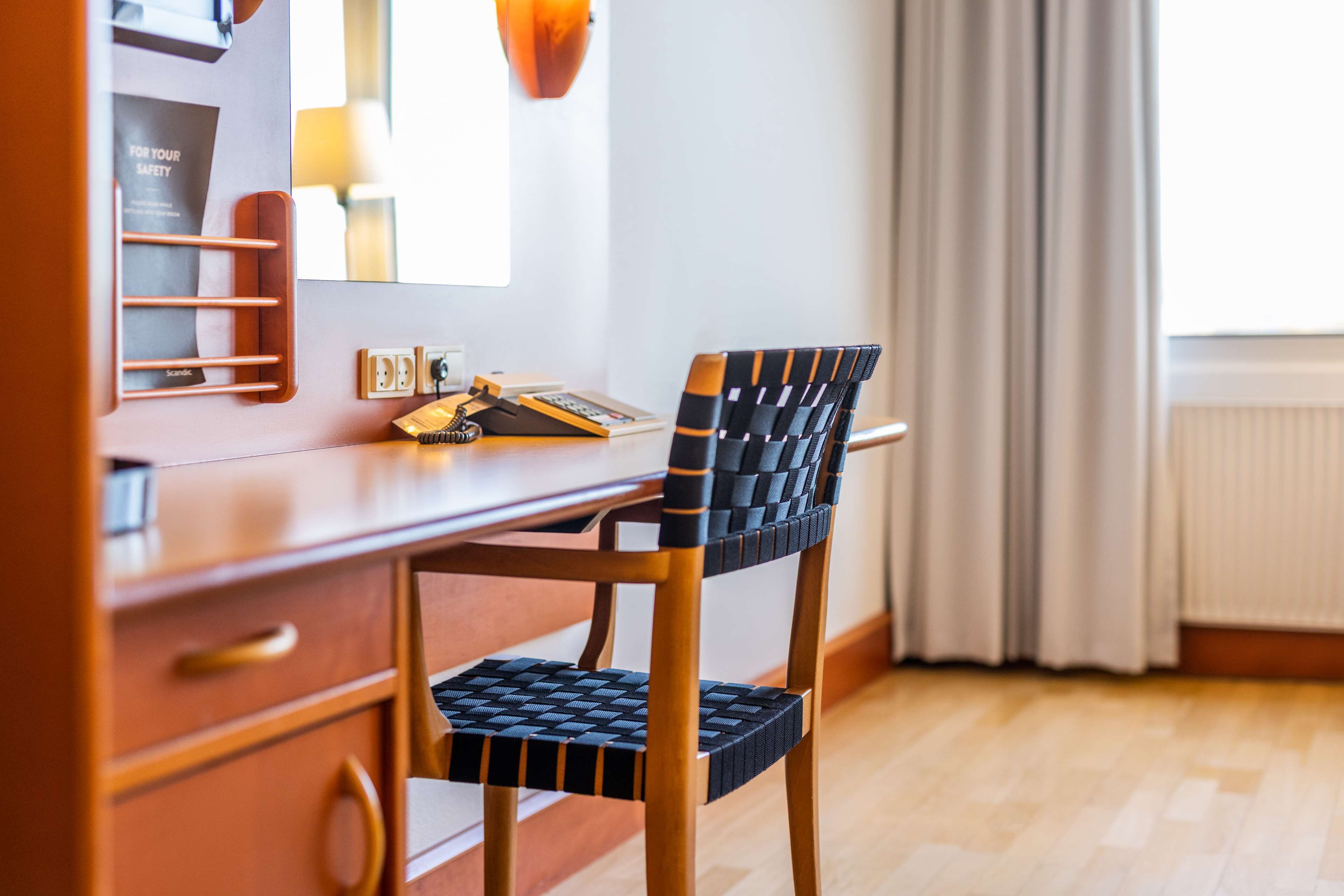 Uma mesa de madeira com cadeira de vime, um espelho e uma janela com cortinas.