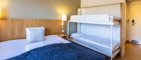 Una habitación de hotel con una cama individual, una cama literera, una lámpara de noche y un cabecero de madera.