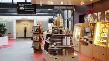 A modern hotel lobby with a wooden reception desk, a coffee shop area, and a conference room.