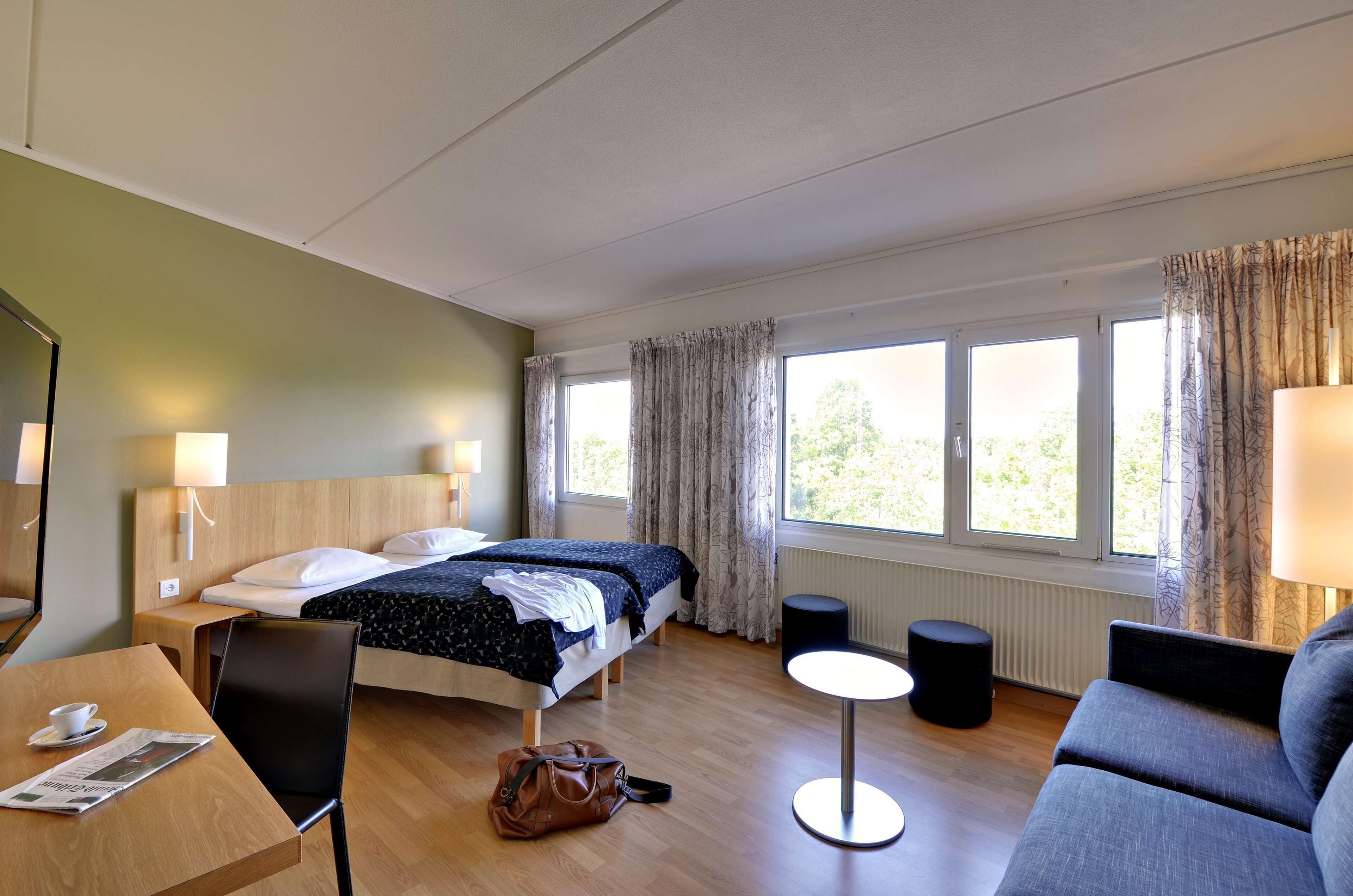 Una habitación de hotel con una cama, un escritorio con una silla, una mesa redonda y un sofá.