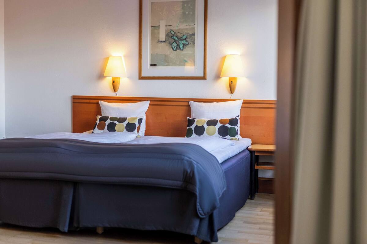 A hotel room with a large bed, two bedside lamps, and a framed artwork on the wall.