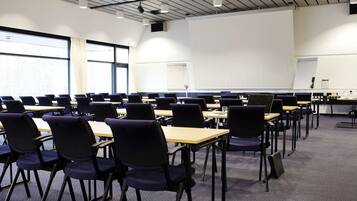 A classroom with rows of desks and chairs, large windows, and a projector screen.