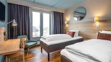A hotel room with two beds, a desk, a chair, a lamp, and a view of the outdoors.