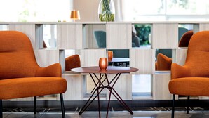 A modern lobby with two orange chairs, a round table, and a vase of flowers. - Scandic Roskilde Park (Roskilde)