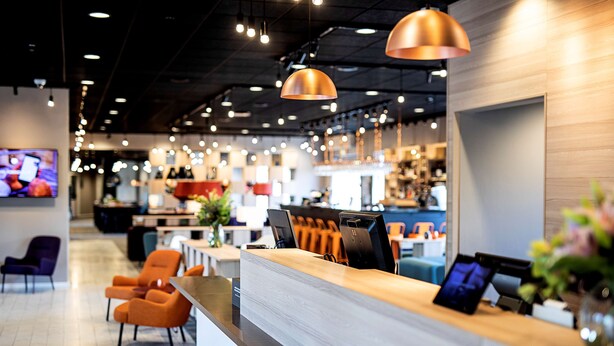 A modern interior with a reception desk, seating area, and a television screen. - Scandic Roskilde Park (Roskilde)