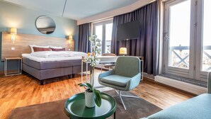 A modern hotel room with a bed, a desk, a chair, a TV, and large windows. - Scandic Roskilde Park (Roskilde)
